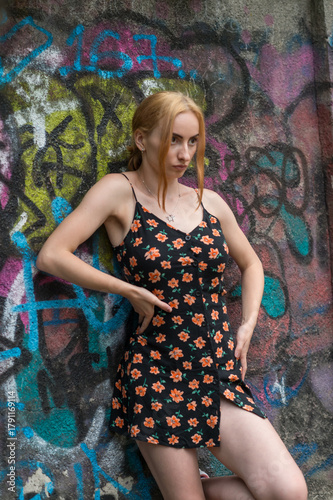 Blonde sensual woman with long legs posing confidently in front of a colorful graffiti wall, wearing a short floral dress. Urban fashion meets vibrant street art in this expressive portrait.