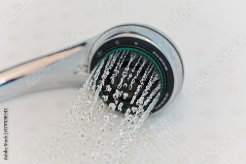 Water Dripping from Chrome Shower Head Against White Tiles