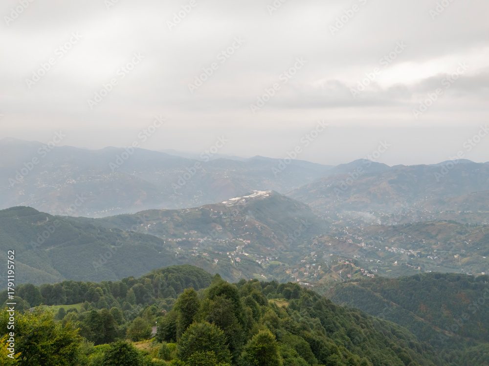 Fototapeta premium Scenic wide-angle view of a densely forested valley and mountain range in the Black Sea region of Turkey, with a small town or village nestled among the hills under a cloudy sky.