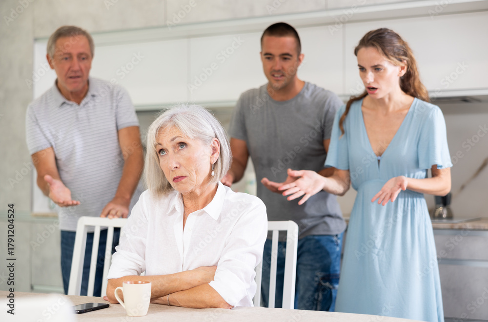 Fototapeta premium Woman sits at table in kitchen and pretends not to understand her family