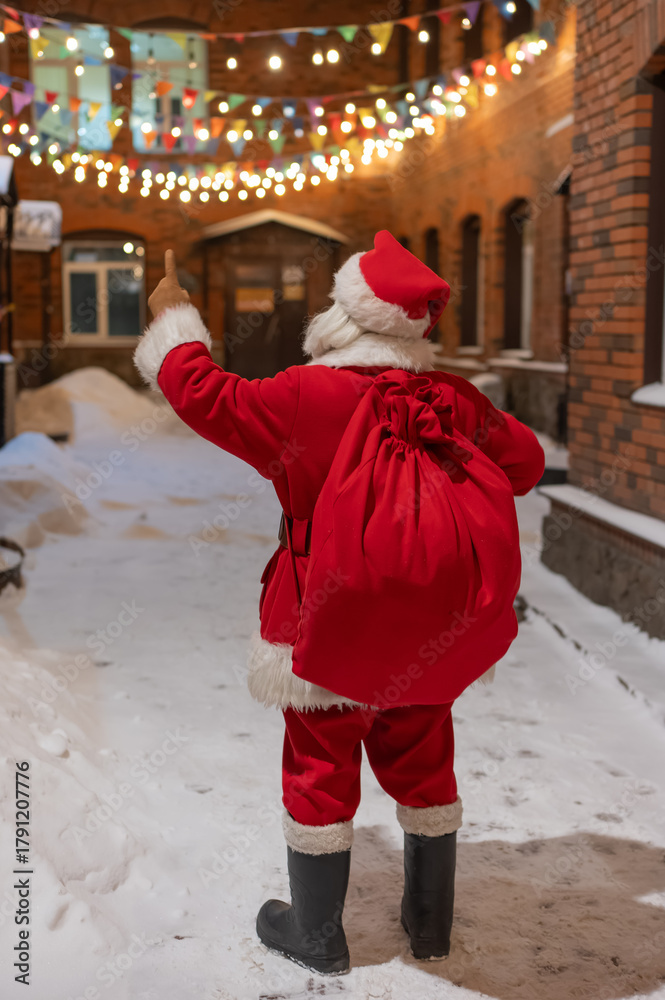 Obraz premium Rear view of santa claus carrying sack of gifts along decorated street. 