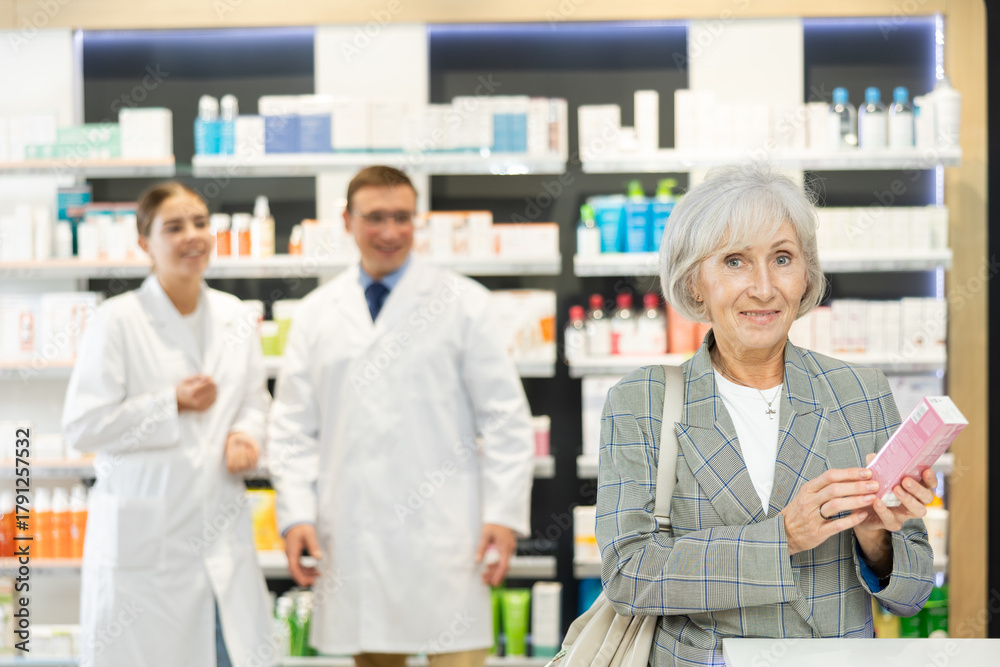 Obraz premium Near self-service window in pharmacy, senior female customer chooses cream for aging skin, carefully reads information for consumer on packaging of product