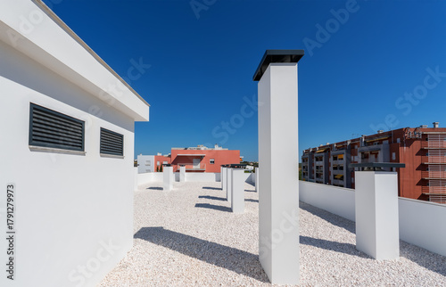 Fotografija A rooftop view featuring several white chimneys against a vibrant blue sky, surr
