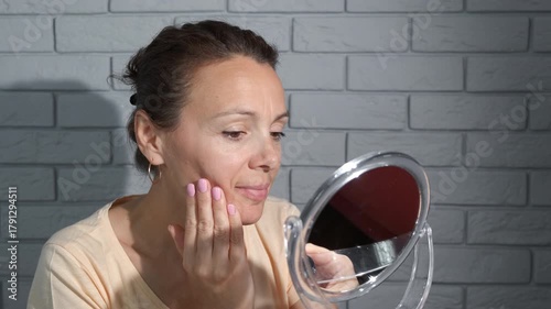 Female doing anti wrinkle procedure against mirror. A view of happy female stand by the mirror and apply the cream at home