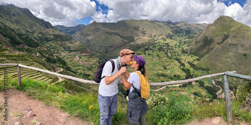 A White Man and a Latin Woman Bite into an Apple at the Same Time, while Holding Hands on a Vegetation Surrounded Trail Overlooking the Mountains at the Archaeological Complex of Incas in Pisac, Peru