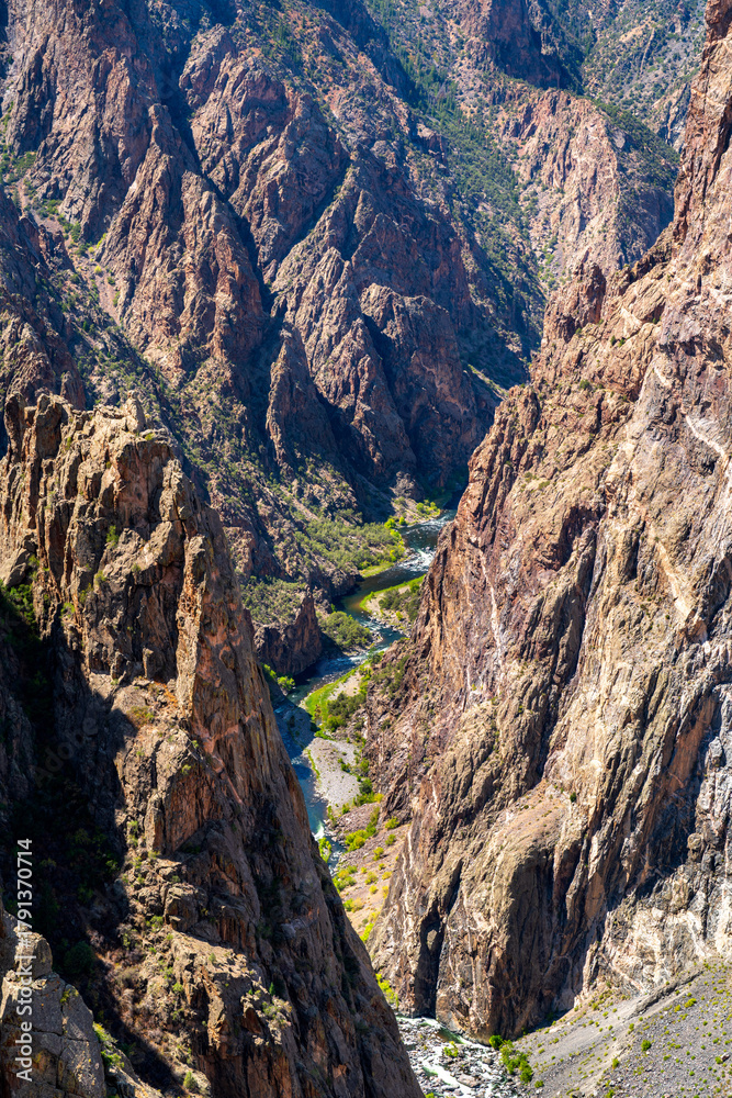 Fototapeta premium Vertical view looking down at the Gunnison River flowing through the deep, narrow Black Canyon. Steep granite cliffs cast shadows on the water