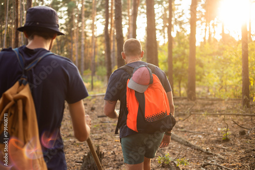 two travellers  with backpacks hiking into the woods at sunset forest