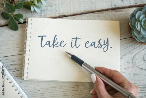 Person writing the phrase Take it easy on a notebook