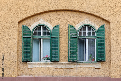 Two windows with wooden green shutters in niche