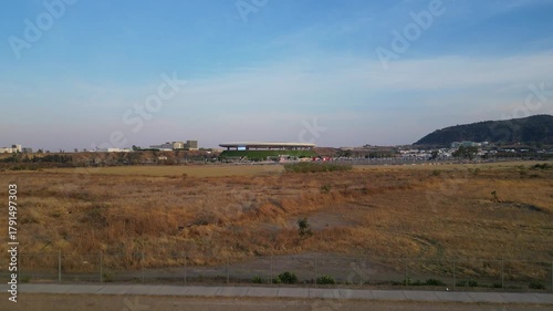Aerial drone lift-off showing distant Akron Stadium surrounded by dry terrain and urban area