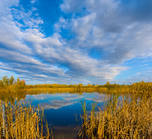 small calm lake among dry autumn prairie under a blue cloudy sky, seasonal outdoor landscape