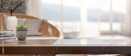 Fototapeta Naklejka Na Ścianę i Meble -  Book and plant aside vase on glass top wooden table across glass wall window in bright living room.
