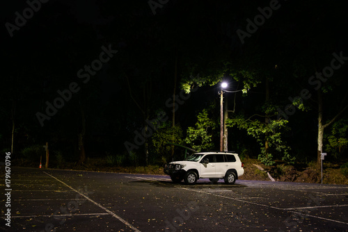 A lone white 4WD car under a street light in an empty parking lot at night - horizontal
