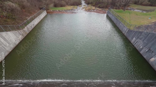 A damn moving water into a small creek. Daytime. Cloudy day.