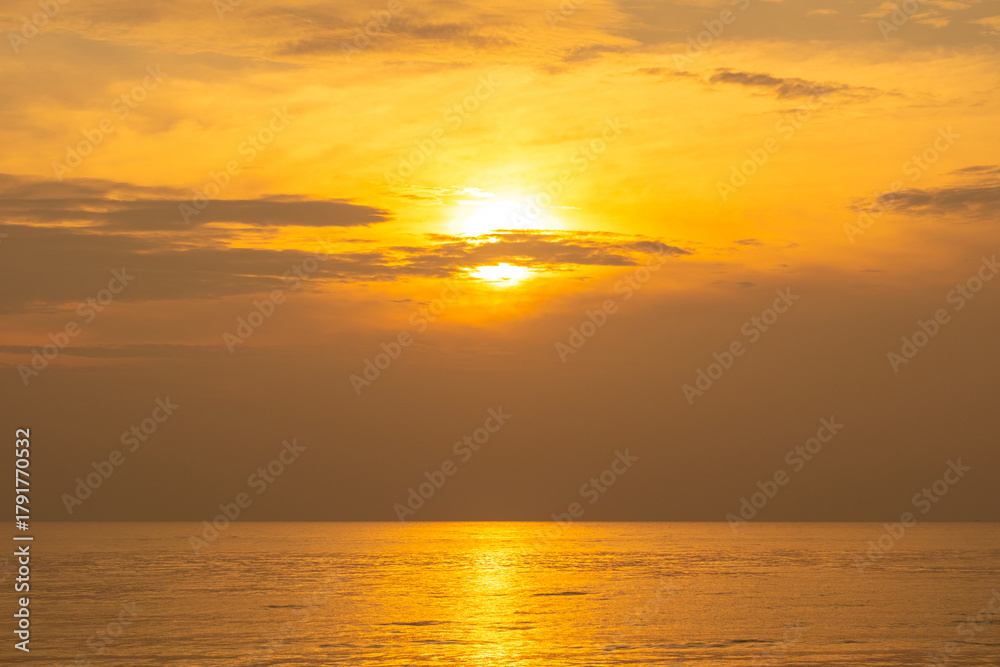 Fototapeta premium Nature sky breathtaking golden sunset over a calm ocean, with the entire sky and water bathed in brilliant shades of yellow and orange. Streaky clouds enhance the dramatic display of light 