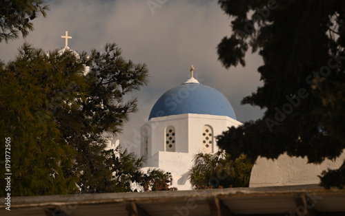 The national flag of Greece flying in front of a blue church steeple.