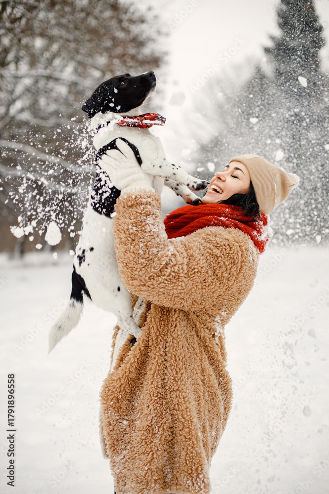 Naklejka premium Woman standing at winter park and holding a black dog