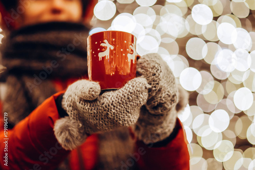Wallpaper Mural Young woman in winter gloves holding a mug of hot tea or wine outdoor, Christmas lights in the background Torontodigital.ca