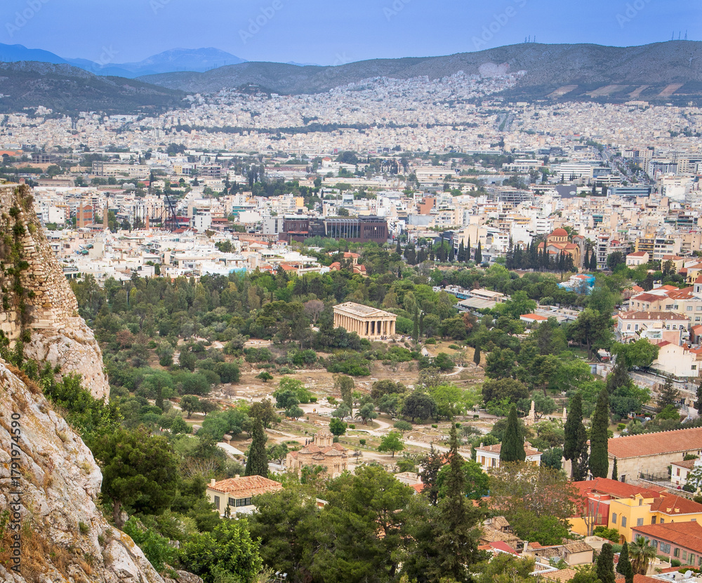 Fototapeta premium View of the Temple of Hephaestus and the Ancient Agora surrounded by greenery, with the modern Athens cityscape in the background