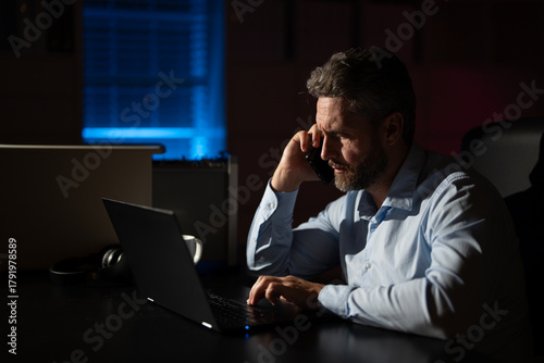 Tired businessman concentrating on career tasks late in the evening. Employee frustrated by workload and approaching deadlines. Entrepreneur working on a startup while bored and stressed.