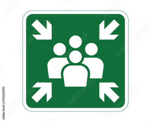 A green square sign displays a white graphic of a group of people with four white arrows pointing inward from the corners, indicating a designated meeting point for assembly.