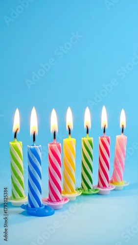 Colorful birthday candles in a row, each with a lit flame, set against a bright, solid blue background