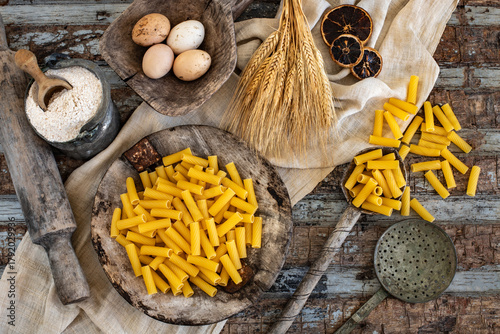 Different types of uncooked pasta on rustic wooden table, in the spoons, cutting board and bowls 