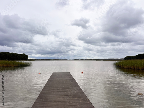 Wooden pier stretches into the lake under cloudy sky.