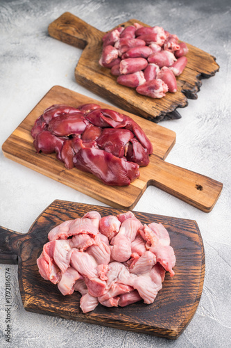 Assorted raw giblets including hearts, liver, and gizzards on vintage wooden boards, organic poultry cooking concept.