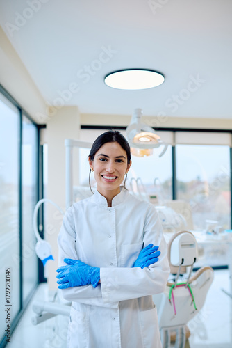 фотографія Female dentist wearing white uniform and blue gloves, smiling and posing with ar