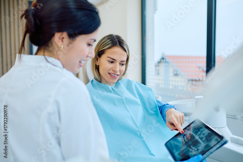 Photos Dentist explaining dental x-ray results on a tablet to a female patient during a