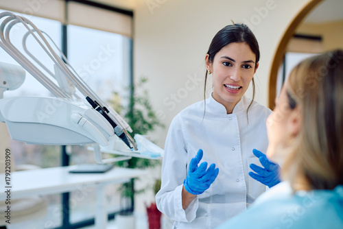 Young woman dentist consulting patient about oral health in a modern dental office, advising on checkup and hygiene
