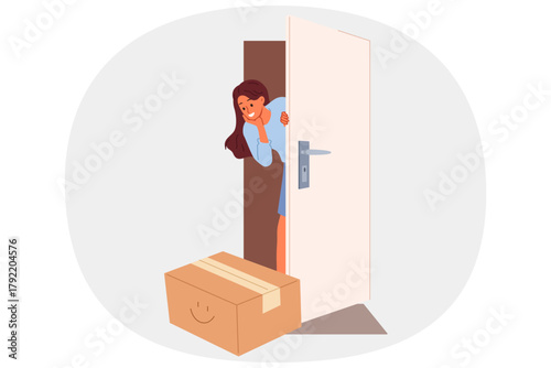 Woman rejoices at receiving package delivery by courier and looks out of apartment through open door. Targeted delivery from online store evokes positive emotions in girl who loves internet shopping