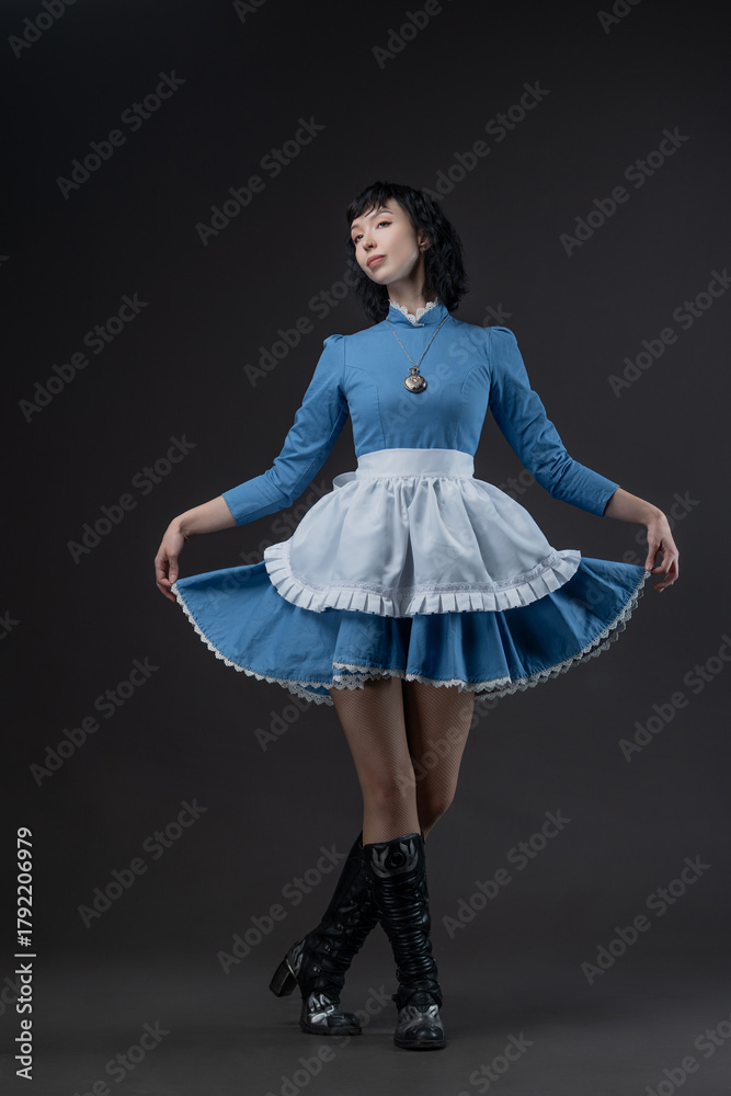 Naklejka premium Costumed Gothic Alice: woman in blue Victorian dress with apron, Wonderland mood.