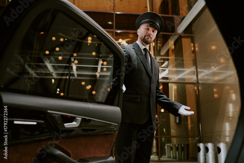 Foto Caucasian middle aged man wearing uniform and cap opening car door with gloved h