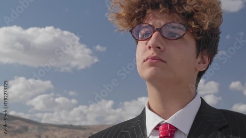 Portrait of a handsome, serious teenager in a business suit against a blue sky.