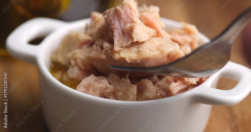 A person takes tuna with a fork from a white ceramic bowl, detailed view highlighting the texture of the fish, healthy eating, and seafood preparation