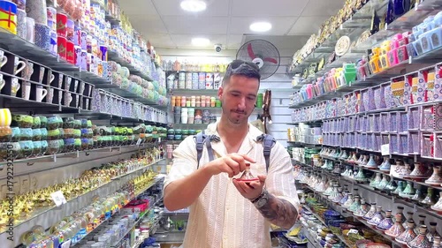 White european young male tourist with a backpack choosing a traditional moroccan tagine in a souvenir store during his vacation in Marrakech's souk looking traditional handicrafts and gifts in Africa