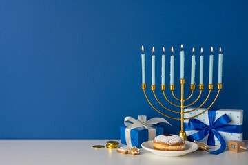 A golden menorah with lit candles sits beside blue gift boxes, a plate with a pastry, coins, and festive decor creating a warm Hanukkah mood on a blue wall