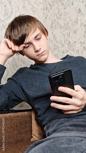 Photography Disappointed sad teenage boy sitting on sofa using smartphone, playing video game