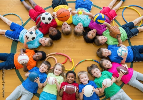 Diverse group of children smiling while holding sports equipment on a gym floor