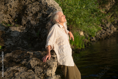 Summer lifestyle portrait senior woman with gray hair relaxes  on the seashore at sunset. Enjoying the little things. spends time in nature in summer.  meditation. banner. greyhairdontcare
