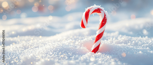 Candy cane with red and white stripes standing in fresh snow  