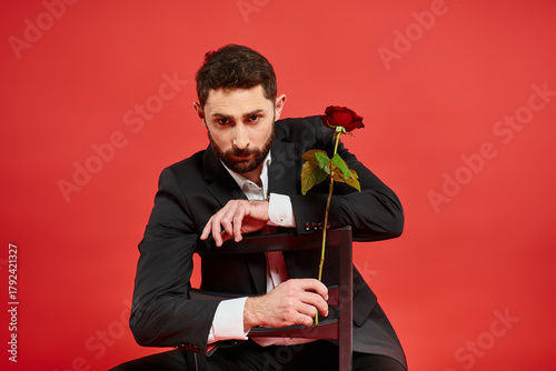 Fotografie Romantic man in elegant suit poses with a rose against a vibrant red backdrop