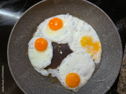 Top-down view of four perfectly cooked sunny side up eggs frying in a nonstick granite-effect pan for a healthy breakfast