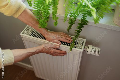 Senior woman warming her hands on a radiator at home, close-up

