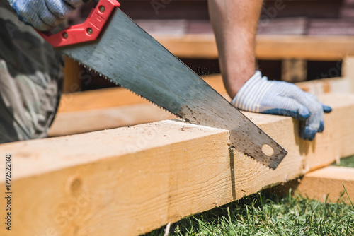 A man sawing a beam with a tool. A hand saw in the hands of a craftsman. Production of wooden products. Construction, wood processing.