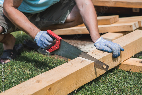 Wallpaper Mural A man sawing a beam with a tool. A hand saw in the hands of a craftsman. Production of wooden products. Construction, wood processing. Torontodigital.ca