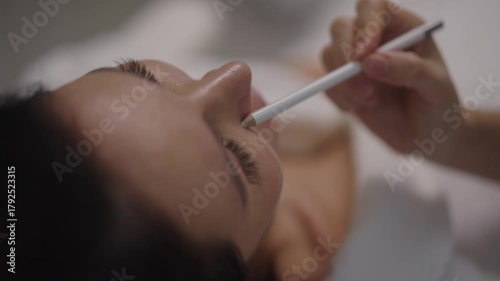 Close-up of professional plastic surgeon or cosmetologist using white pencil to mark lines on female patient face, preparing for cosmetic surgery or aesthetic treatment in modern aesthetic clinic.