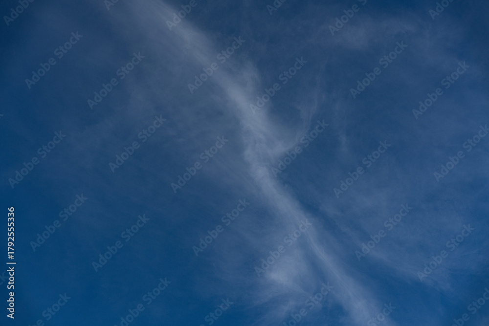 Fototapeta premium Wispy cirrus streaks cross deep blue sky; a minimal skyscape with smooth gradients and airy texture, ideal as clean background, weather concept or lifestyle design with selective focus.